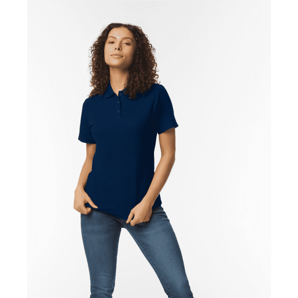A model wearing a navy blue ladies' double pique polo shirt, featuring a logo, paired with denim jeans.