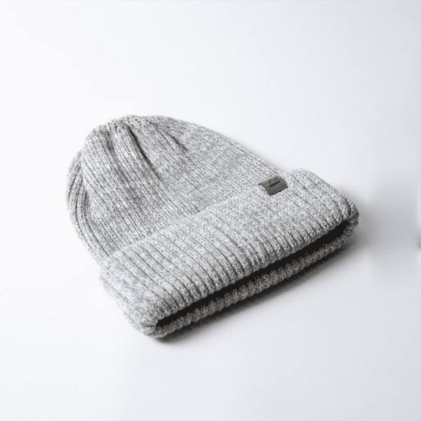 A grey beanie with a rolled cuff, featuring a small logo. It's made from a textured knit material.