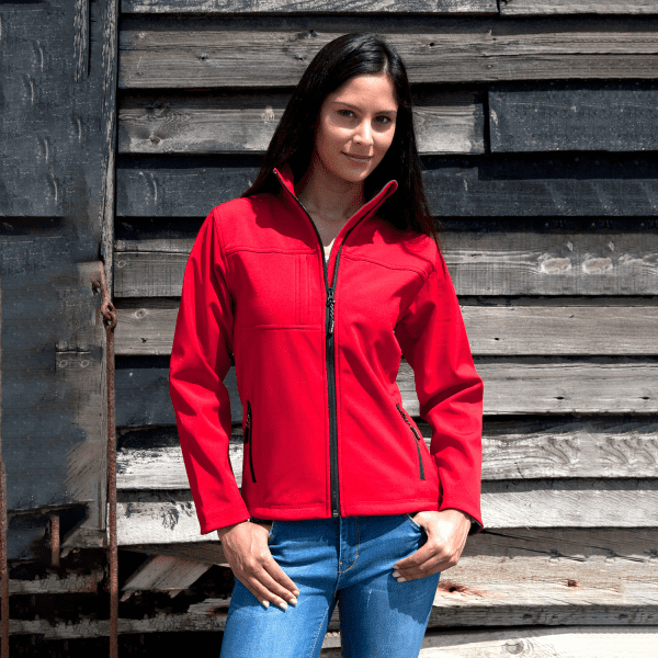 A red ladies classic softshell jacket displayed on a model, featuring a zip front and a logo.