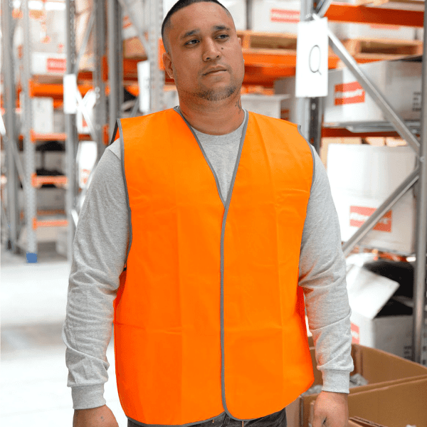 An orange high-visibility safety vest is displayed on a person, set against a warehouse background.