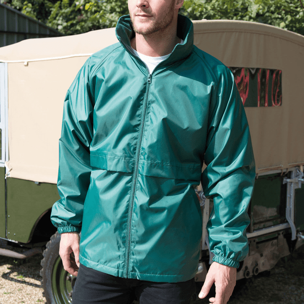 A man wearing a teal rain jacket with a high collar, standing outdoors near a vehicle. The jacket has a logo.