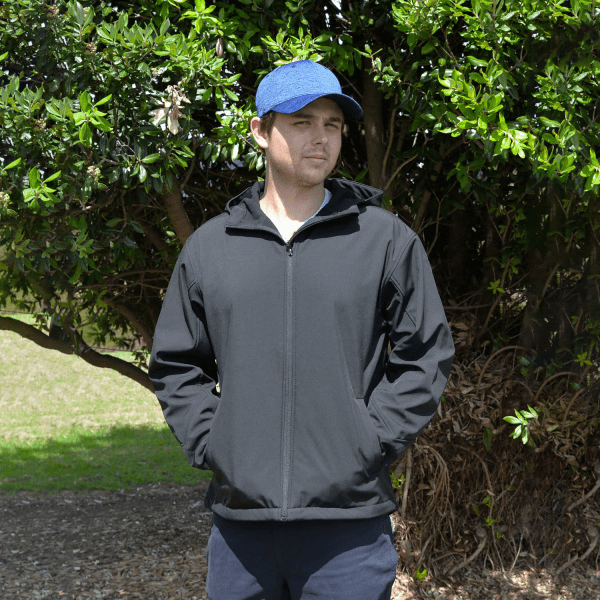 A black softshell jacket featuring a hood, worn by a person outdoors. The individual is also wearing a blue cap.