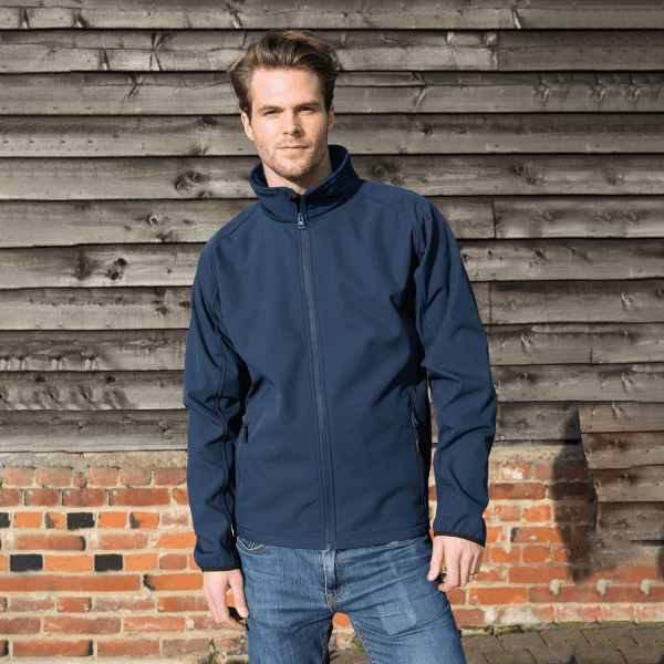 A navy softshell jacket with a high collar, featuring a front zipper and an unseen logo, worn by a model.