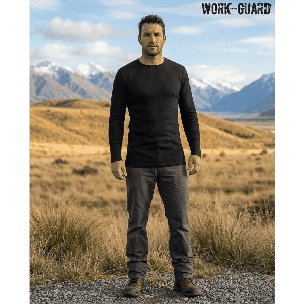 A man stands outdoors wearing a black long-sleeve thermal shirt and grey trousers, with mountains in the background.