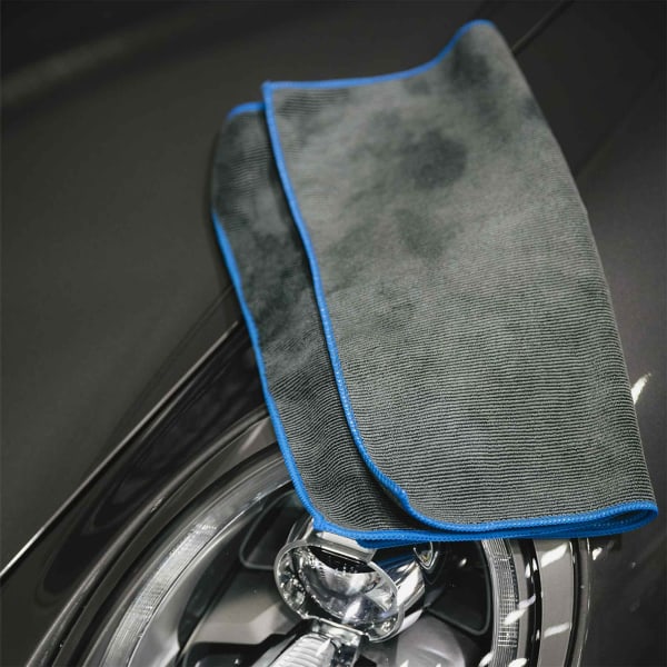 A grey cooling towel with blue trim laid on a shiny surface, featuring a circular chrome element in the background.