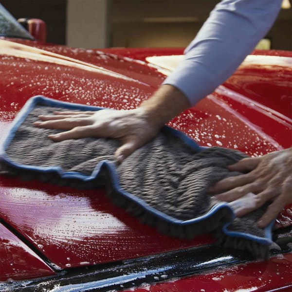 A grey towel with blue trim being used to dry a red car, displaying a textured surface.