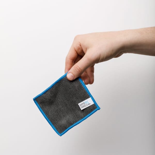 A hand holding a grey and blue Rapid Dry micro towel, designed as a compact hand towel.