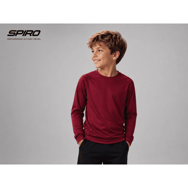 A young boy wearing a maroon long-sleeve shirt, featuring a logo, with a neutral background.