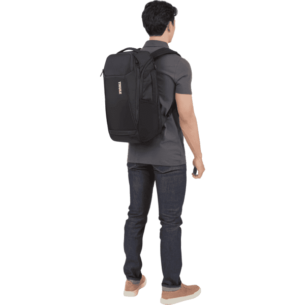 A black Thule Accent Backpack 28L is worn on the back of a person standing casually.
