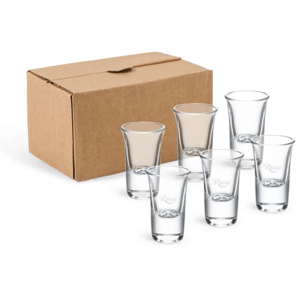 A set of six clear glass shot glasses displayed in front of a brown cardboard box.