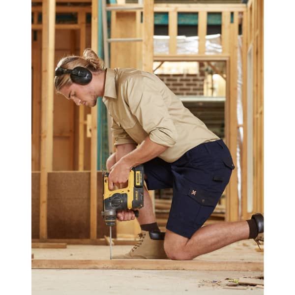 A man in khaki and navy work shorts operating a drill, wearing ear protection, in a construction setting.
