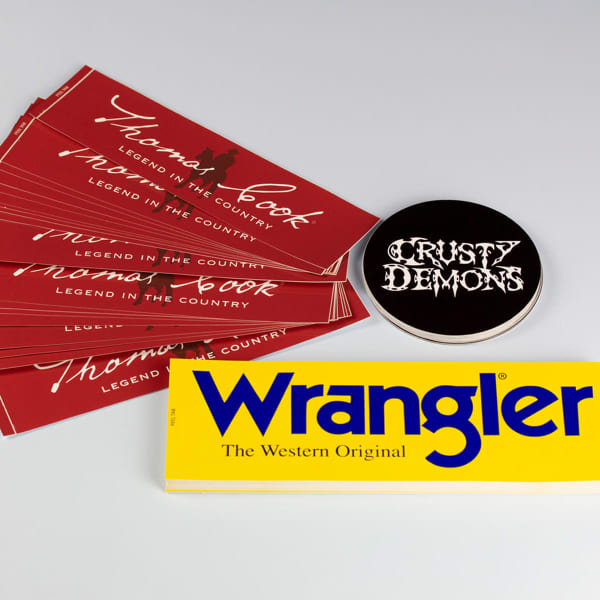 A set of red bumper stickers featuring the text "Thomas Cook," alongside a circular black sticker and a yellow "Wrangler" sticker.