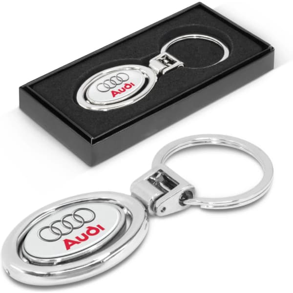 A silver metal key ring with an oval design, presented in a black box, featuring a logo.