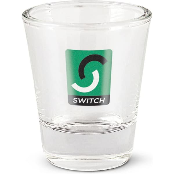A clear glass shot glass with a logo, featuring a thick base and a smooth rim.