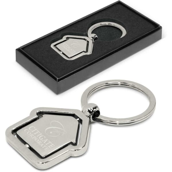 A metal key ring shaped like a house, presented in a black box with a logo on the key ring.
