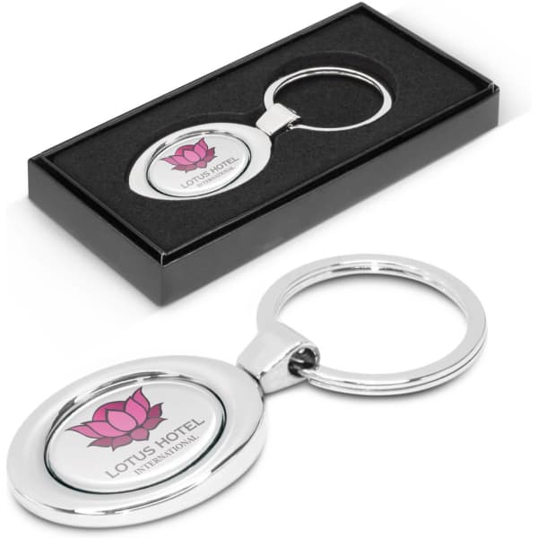An oval metal key ring in a sleek black gift box, featuring a logo with a pink lotus design.