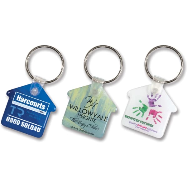 Three house-shaped key rings in various designs, featuring a keychain attachment and different colours. One has a logo.