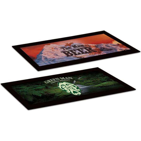 A rectangular black counter mat featuring two designs, one with snow-capped mountains and the other with a green forest scene.