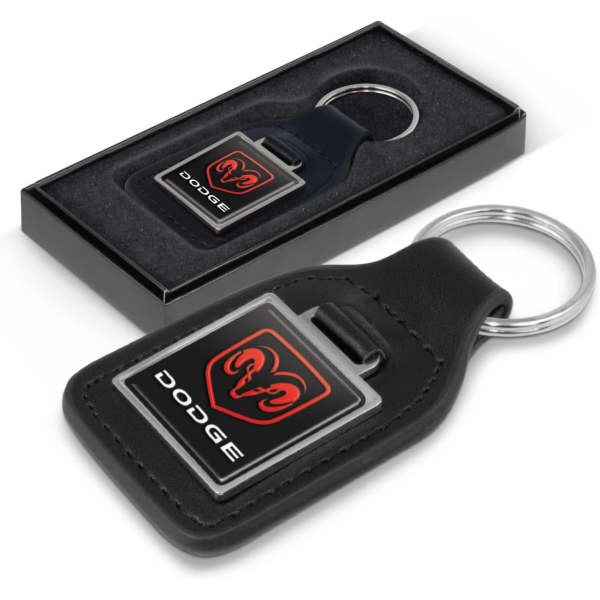 A square black leather key ring with a logo, presented in a black gift box with a grey interior.