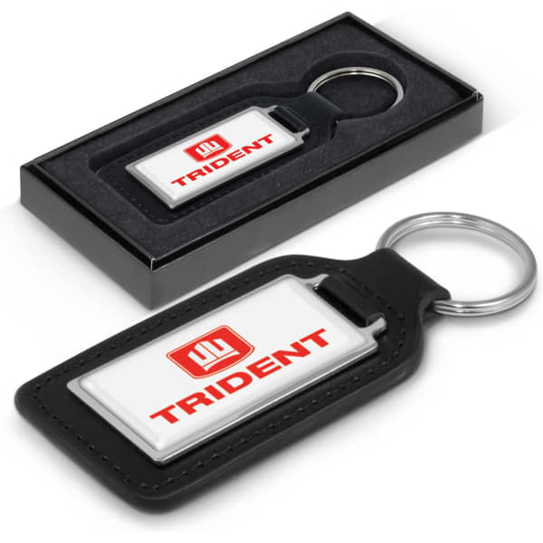 A rectangular key ring in black leather and white with a logo, presented in a black gift box.