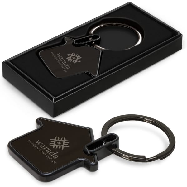 A black key ring in the shape of a house, presented in a black box with a logo.
