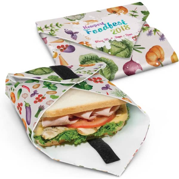 A reusable food wrap featuring a colourful vegetable design, with a sandwich peeking out. Includes a closure strap.
