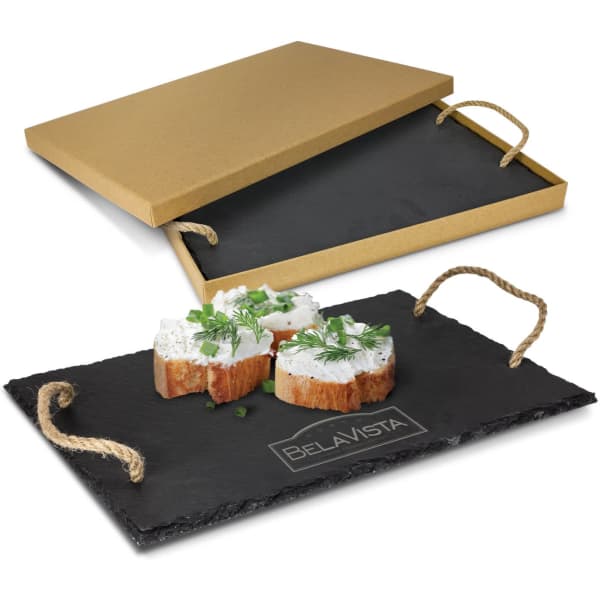 A slate serving board with a rustic design, featuring cheese topped with herbs, and a kraft paper box.