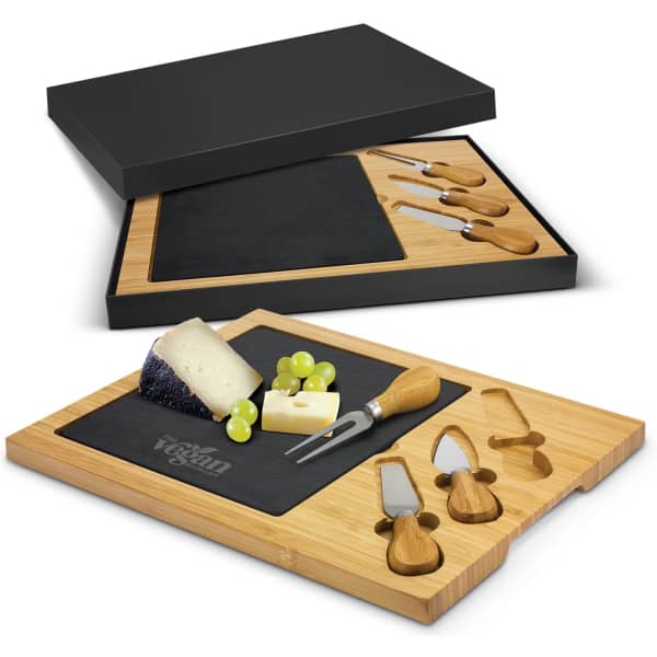 A slate cheese board in a bamboo base with cheese, grapes, and wooden-handled knives, presented in a black box.