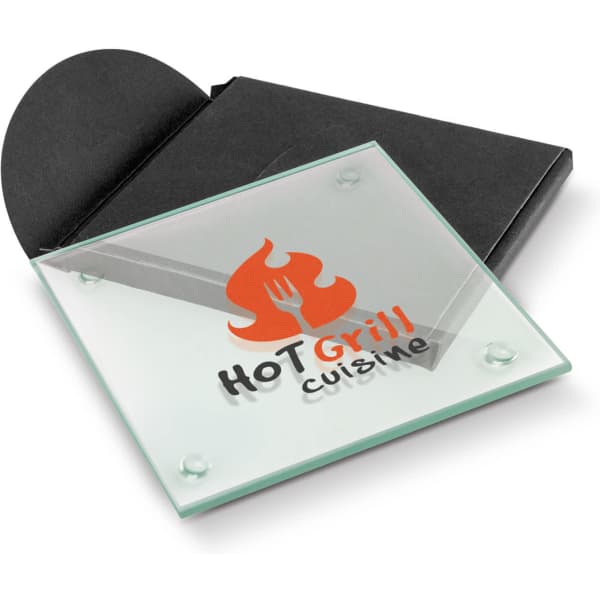 A square glass coaster in green, featuring a logo, packaged in a black envelope.