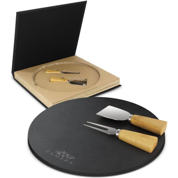 A round black slate cheese board set with two stainless steel cheese knives featuring wooden handles, presented in a black box.