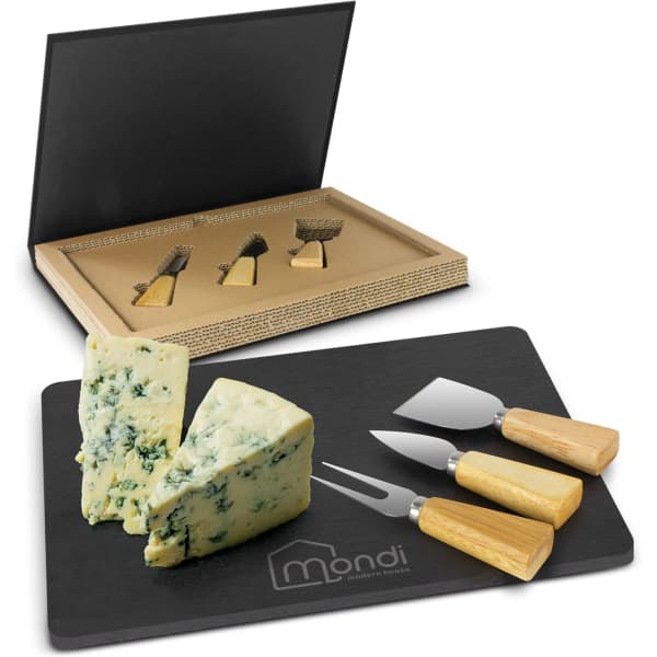 A slate cheese board set with three metal knives, featuring wooden handles, displayed with two pieces of blue cheese.