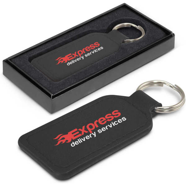 A rectangular black leather key ring with a metal ring, presented in a black box. It features a logo.