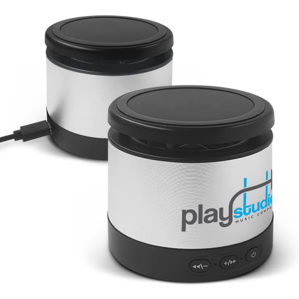 A wireless speaker and charger in silver with a black base, featuring a logo and control buttons.