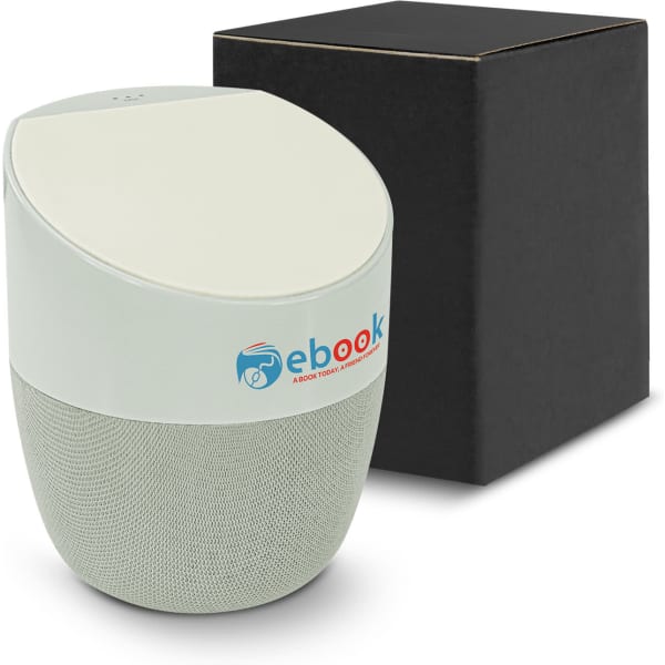 A wireless charger speaker in light green with a fabric base, alongside a black packaging box. It features a logo.