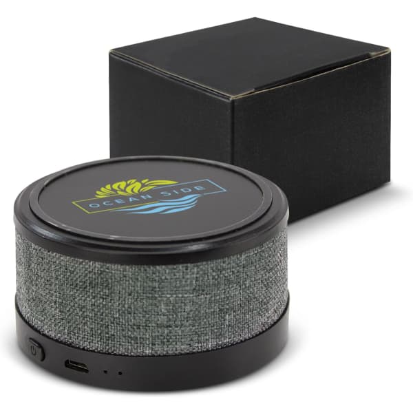A wireless charger and speaker with a grey fabric design, accompanied by a sleek black packaging box.
