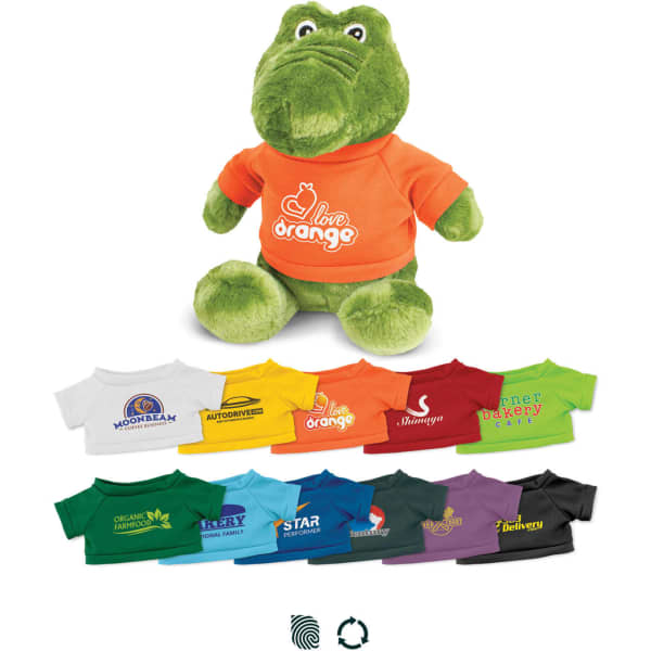 A green crocodile plush toy wearing an orange T-shirt with a logo, accompanied by various smaller T-shirts in different colours.