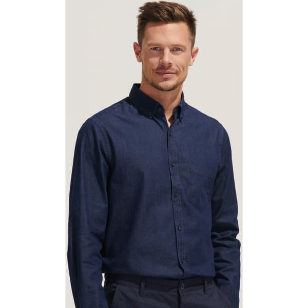 A men's denim button-up shirt in dark blue, featuring a chest pocket and a collar, with a model wearing it.