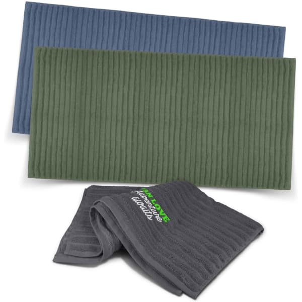 A set of three luxurious bath towels in shades of blue, green, and grey, featuring a logo on one towel.