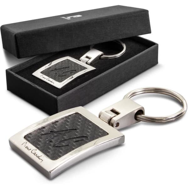 A silver key ring with a textured black insert, presented in a black box with a branding logo.