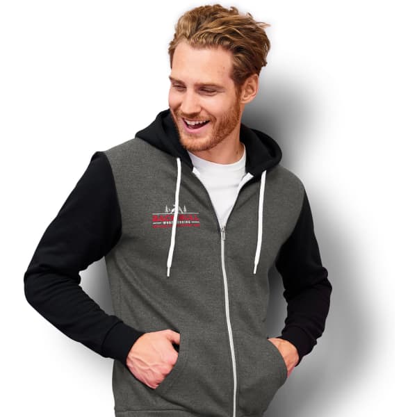 A zipped unisex sweatshirt in grey and black, featuring a logo. The model is smiling and has hands in the pockets.