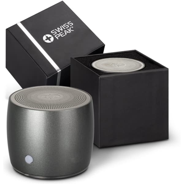 A grey Swiss Peak bass speaker with a round design, displayed next to its black box packaging.