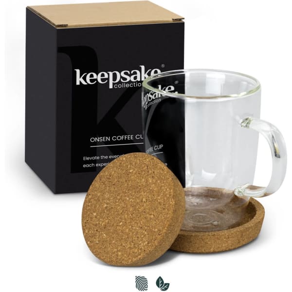 A glass coffee mug with a handle sits on a cork coaster, alongside a black box with branding.