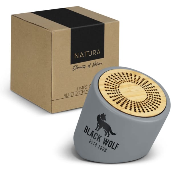 A grey Bluetooth mini speaker with a bamboo top, beside a brown package featuring a logo.