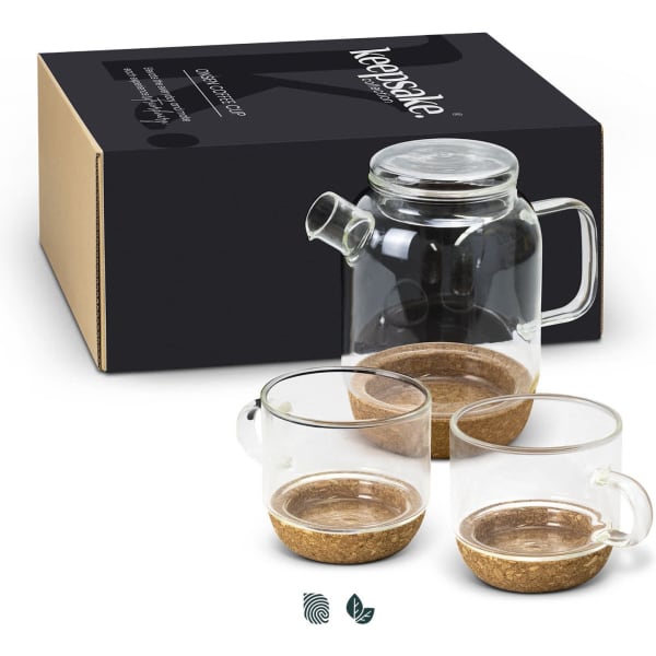 A glass tea pot with a handle and two matching transparent cups, featuring cork bases, presented in a box with branding.
