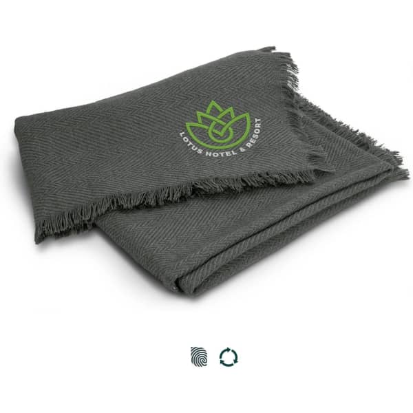 A grey throw blanket with a herringbone pattern and a logo in green, featuring fringed edges.