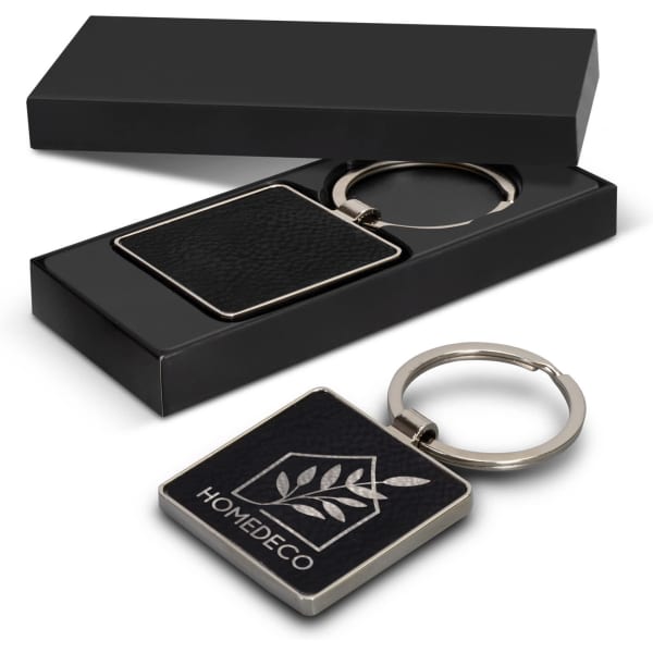 A square black key ring with a silver keychain, packaged in a sleek black box. Features a logo on the key ring.