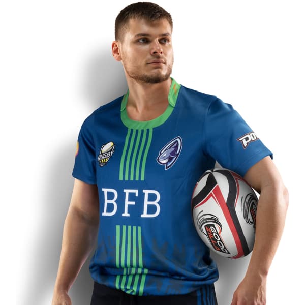 A man in a blue rugby T-shirt with green accents, holding a rugby ball, featuring a logo.