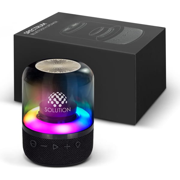 A Bluetooth speaker with a cylindrical design, featuring a coloured LED light base, sitting beside its black packaging.