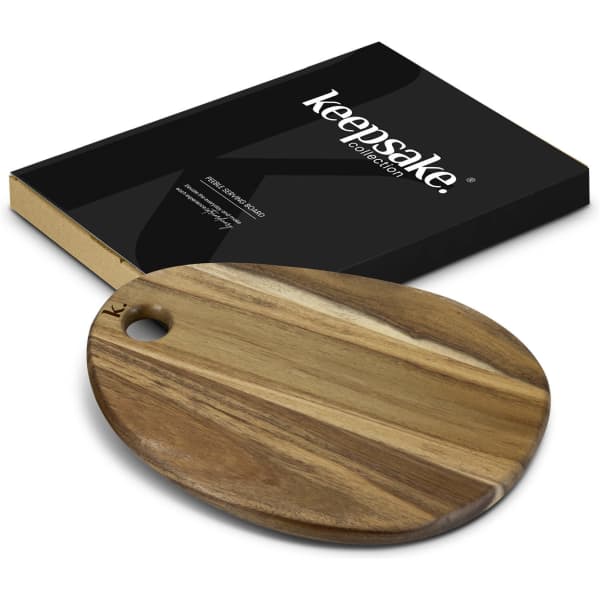 A natural wooden serving board with an oval shape and a hanging hole, next to a black box with a logo.