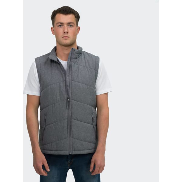 A man stands wearing a grey puffer vest over a white T-shirt, paired with blue jeans. The vest features a logo.